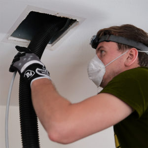 Duct cleaning in Freehold, duct service Freehold technician with vacuum hose in open vent in ceiling
